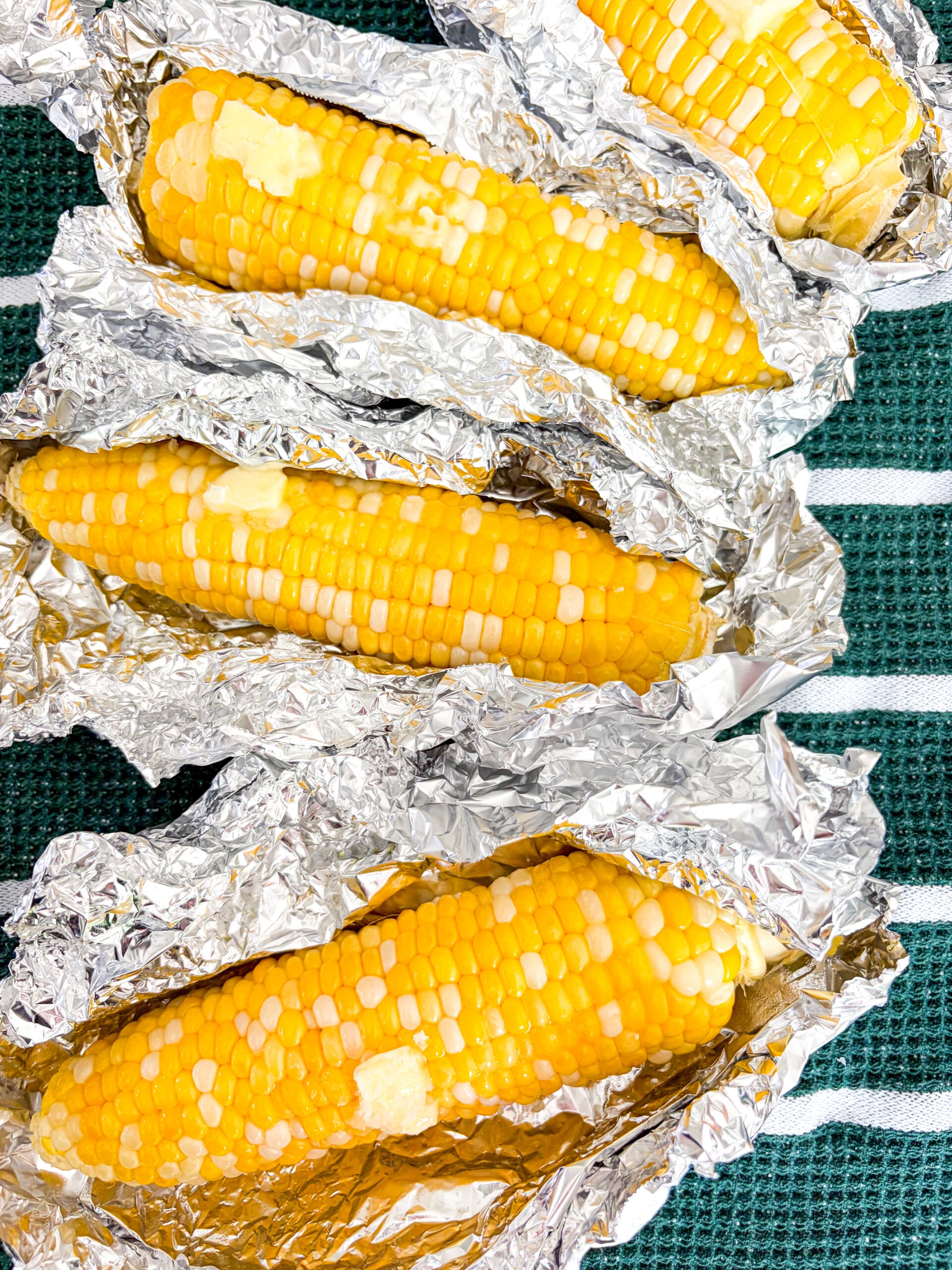 Corn on the cob wrapped in foil packages with butter pads and salt