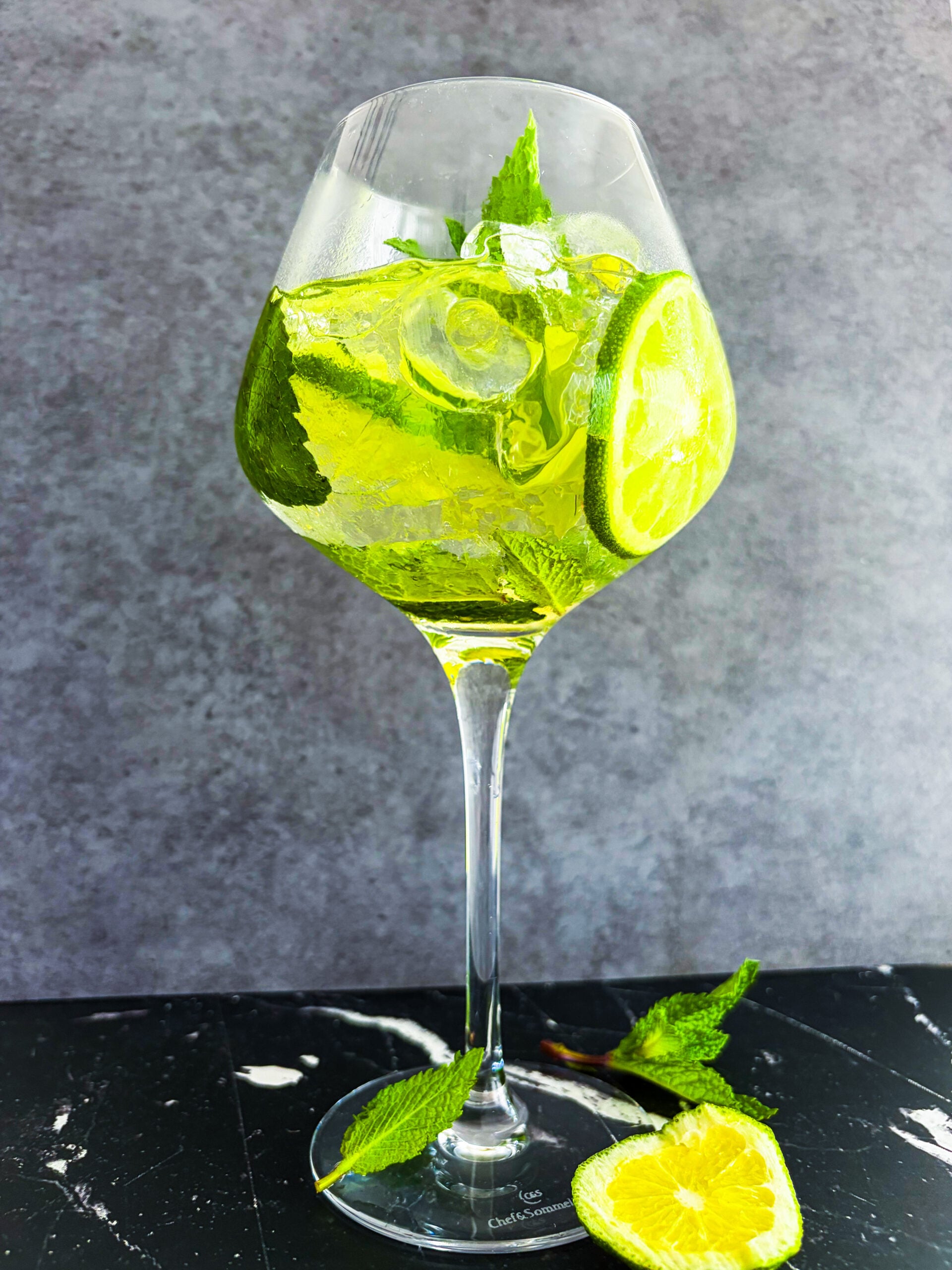 Full shot of Hugo Spritz cocktail next to lime wheel and mint sprigs
