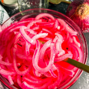Close up of pickled red onions in a glass bowl with a spoon