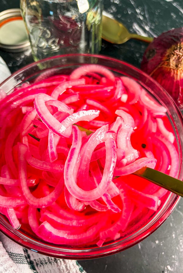 Close up of pickled red onions in a glass bowl with a spoon