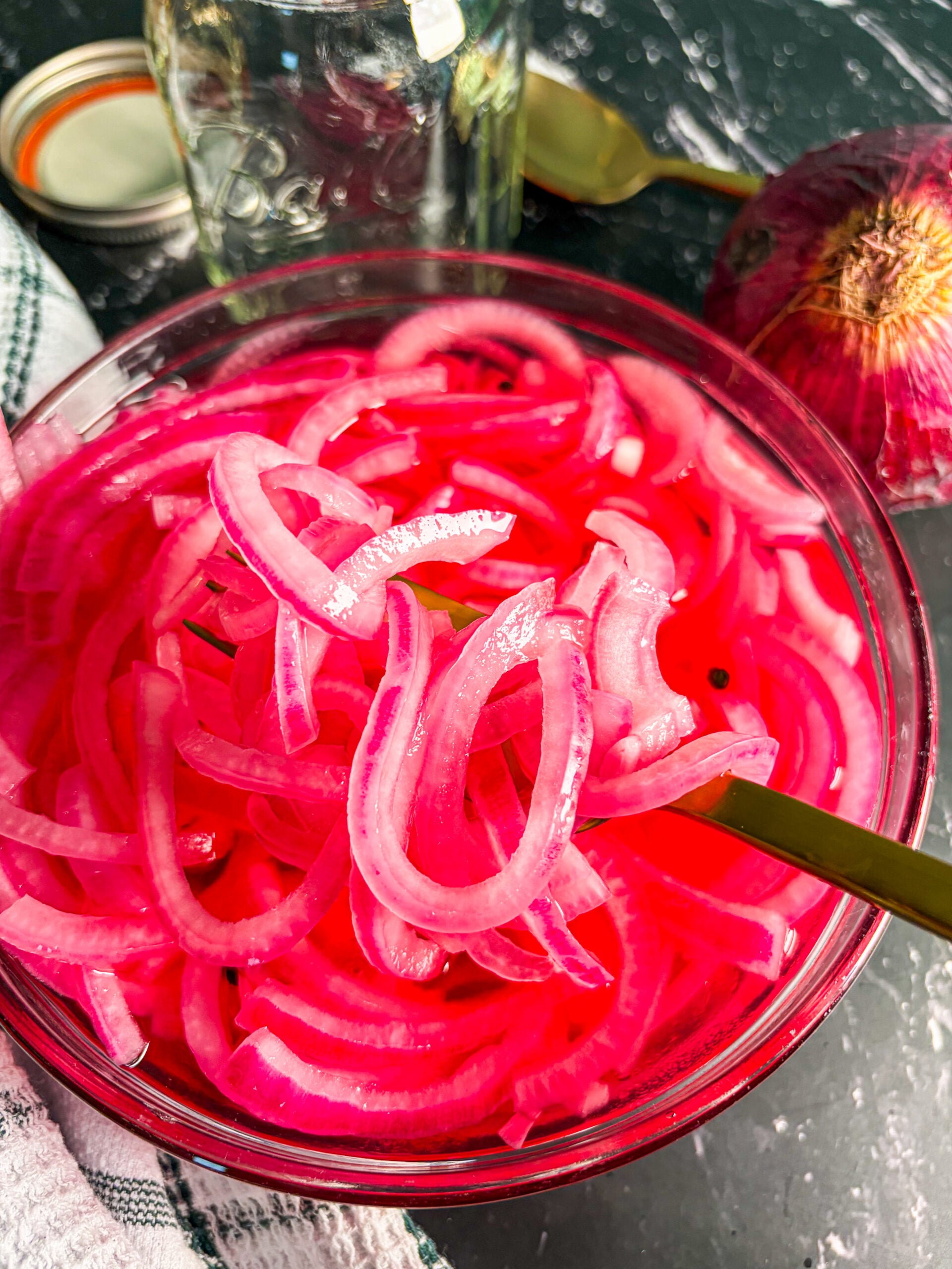 Close up of pickled red onions in a glass bowl with a spoon