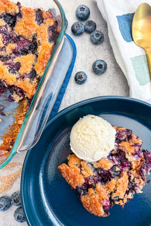 Blueberry cobbler plated with vanilla ice cream next to full cobbler