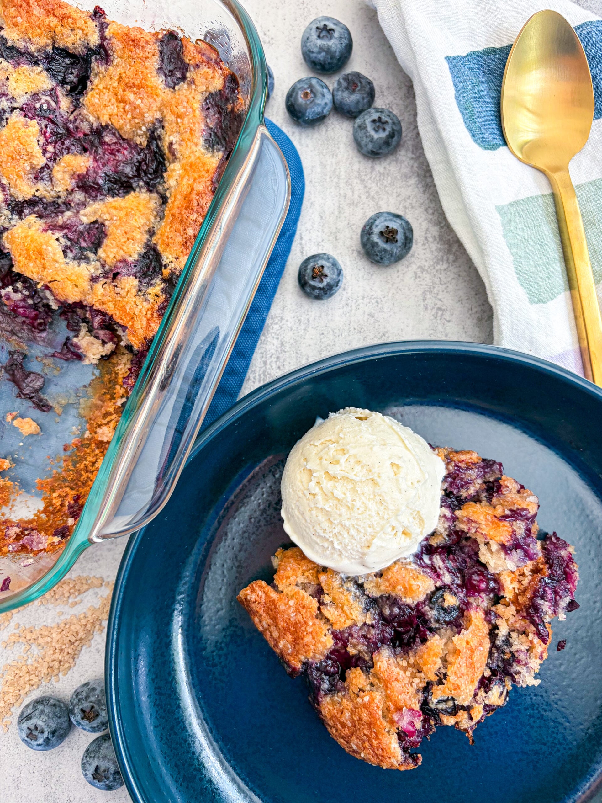 Blueberry cobbler plated with vanilla ice cream next to full cobbler