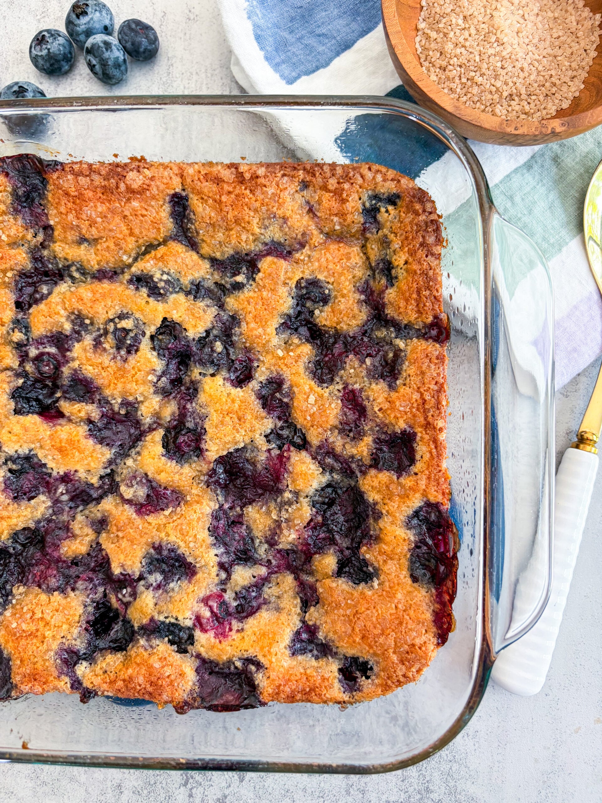 Blueberry cobbler in glass baking dish next to serving spoon