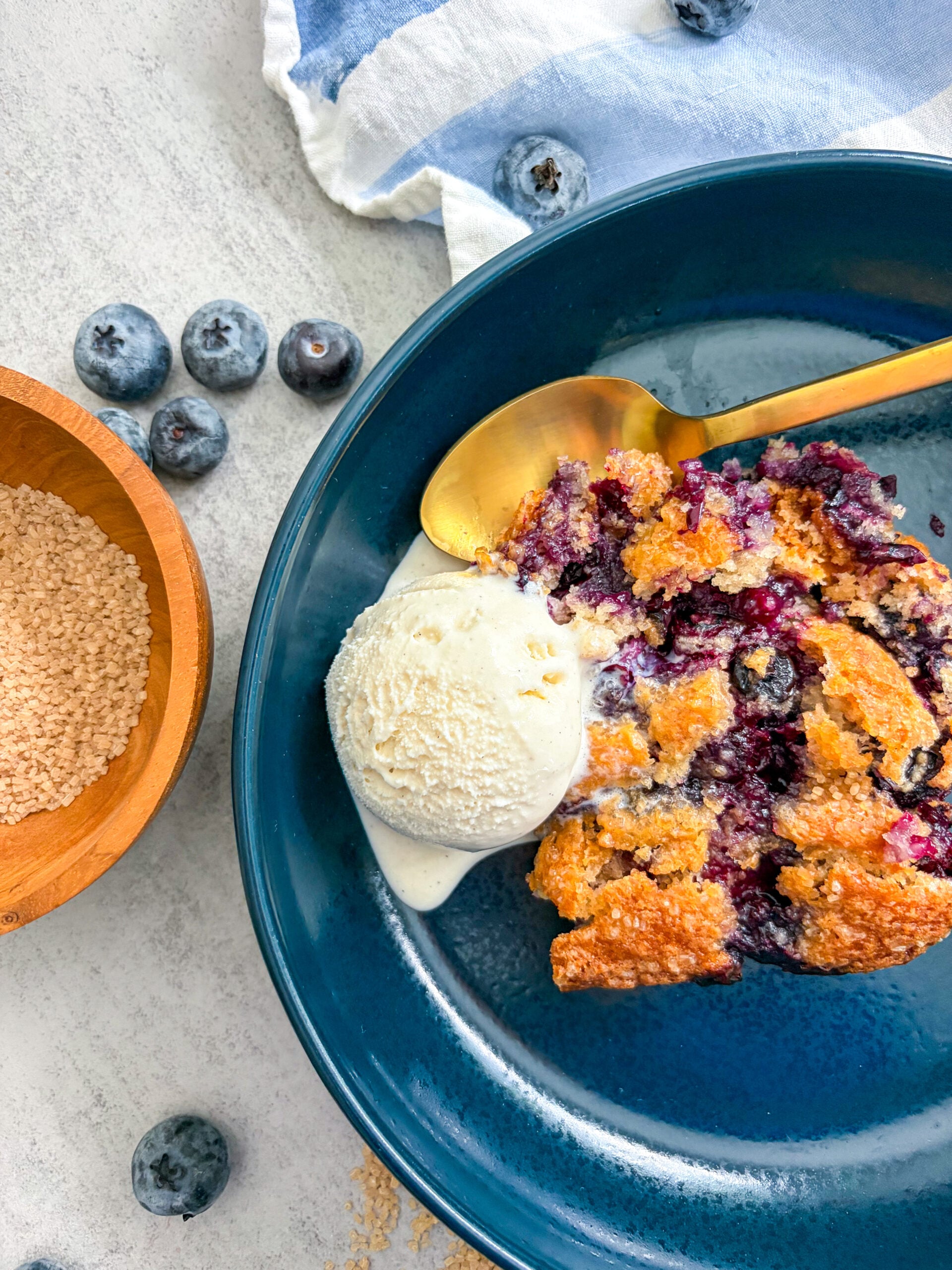 Close up of blueberry cobbler in a blue bowl with vanilla ice cream and a spoon