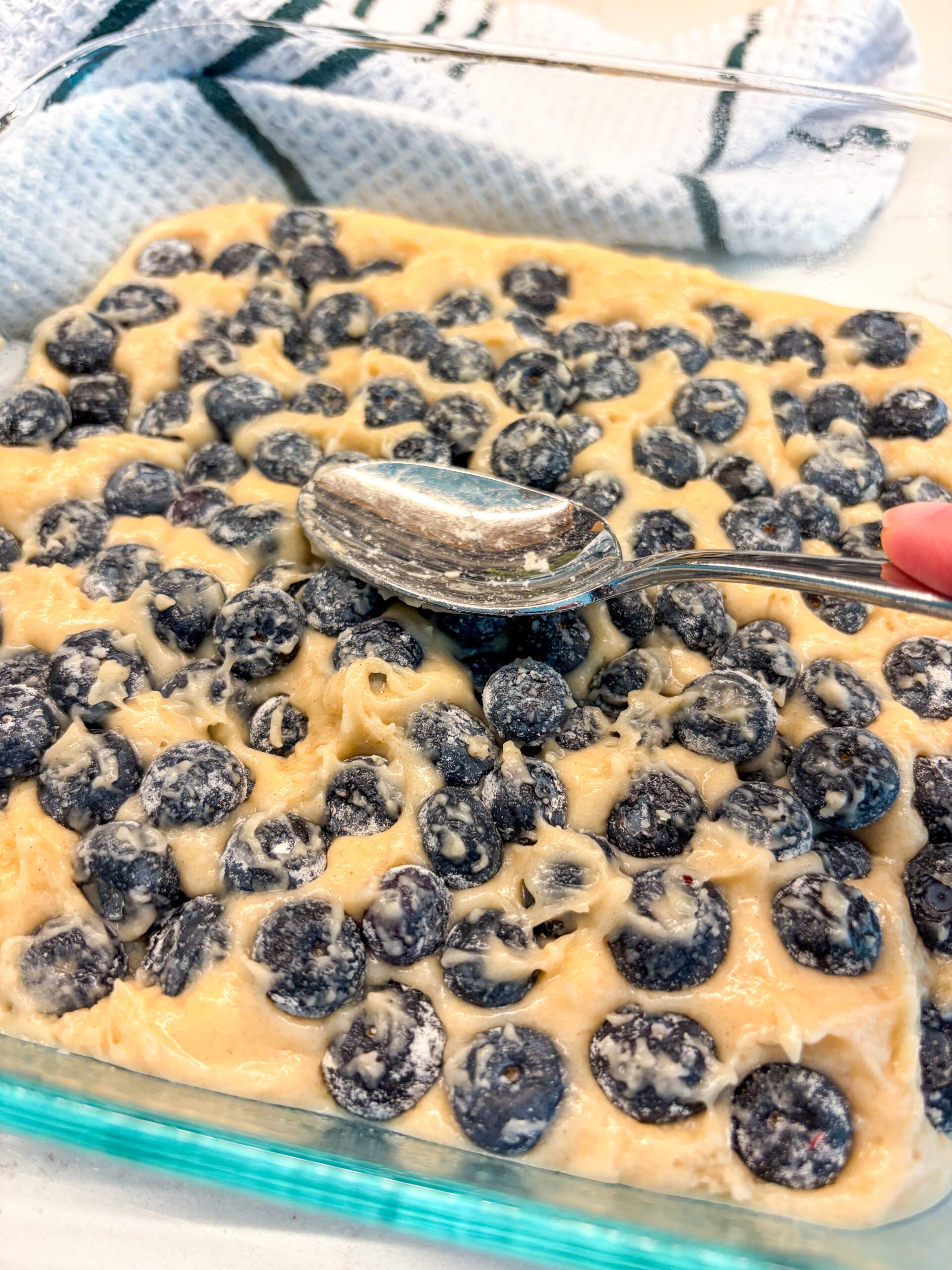 Blueberries added and pressed down with back of spoon to cobbler batter in a pan