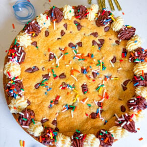 Frosted cookie cake with sprinkles and next to gold candles and blue ribbon