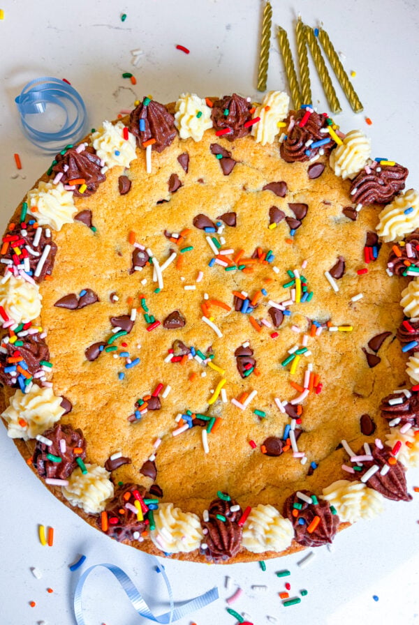Frosted cookie cake with sprinkles and next to gold candles and blue ribbon