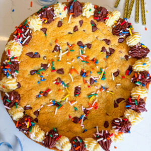 Frosted cookie cake with sprinkles and next to gold candles and blue ribbon
