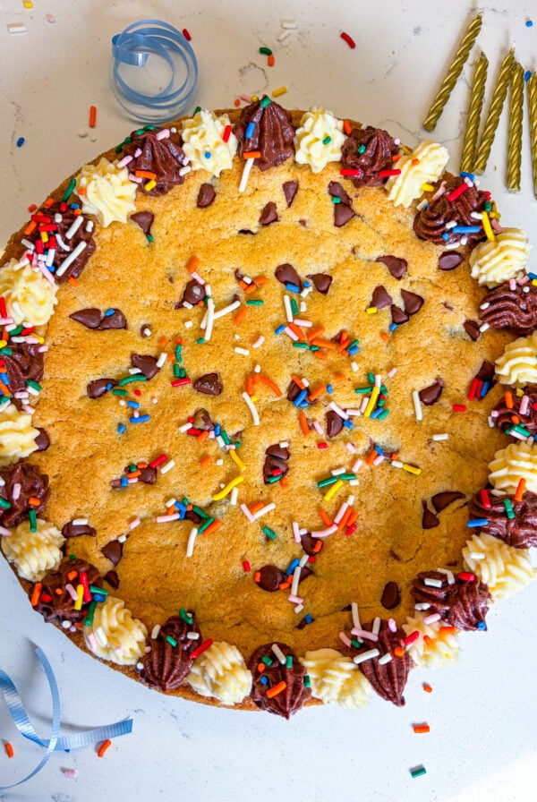 Frosted cookie cake with sprinkles and next to gold candles and blue ribbon