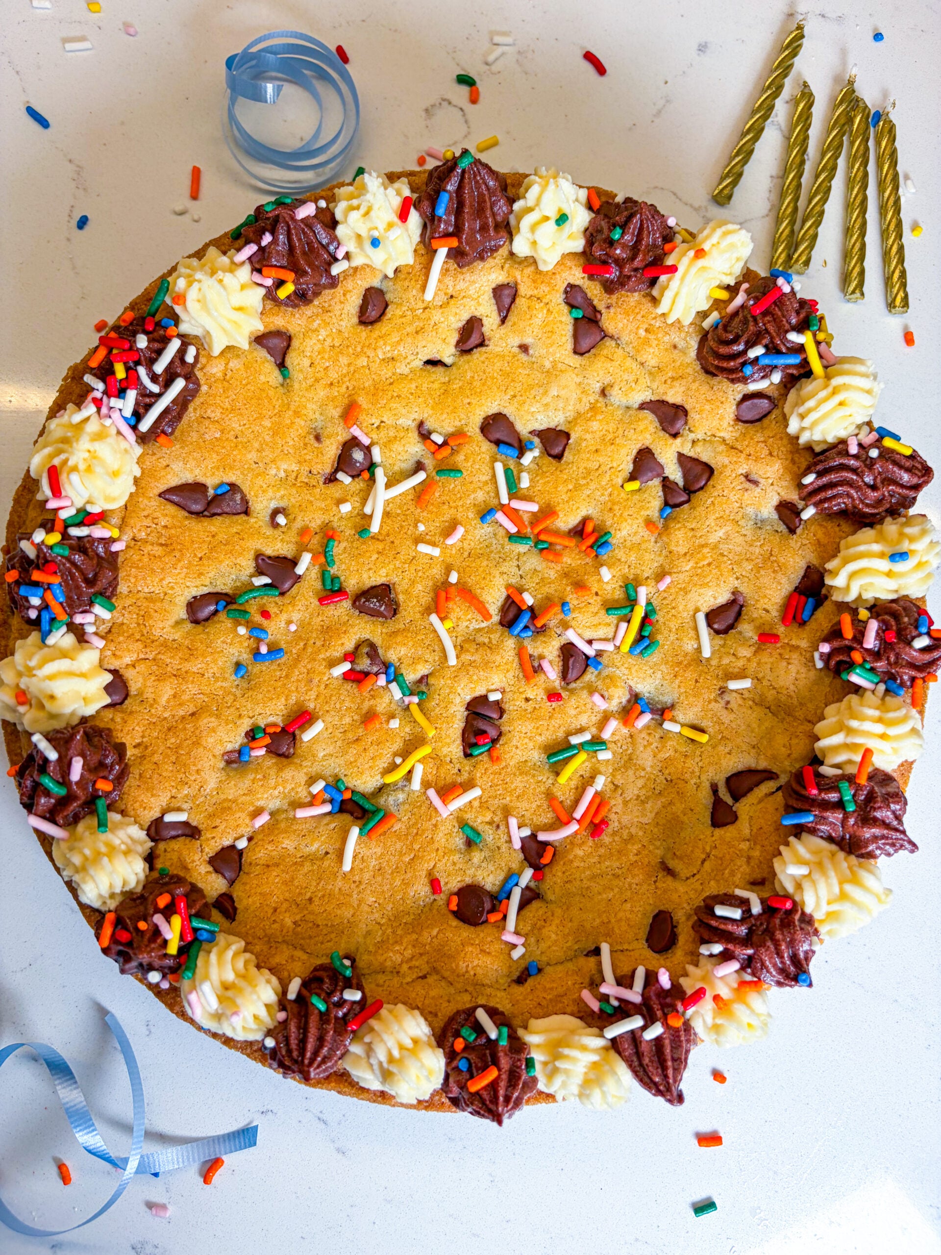 Frosted cookie cake with sprinkles and next to gold candles and blue ribbon