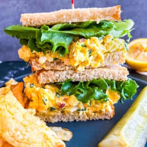 Egg salad sandwich on a plate with pickle and chips
