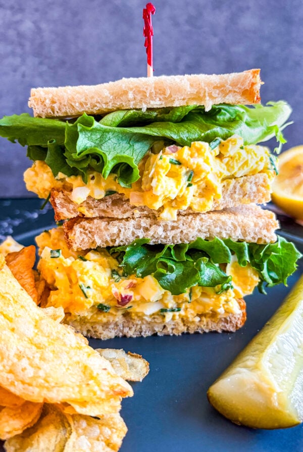 Egg salad sandwich on a plate with pickle and chips