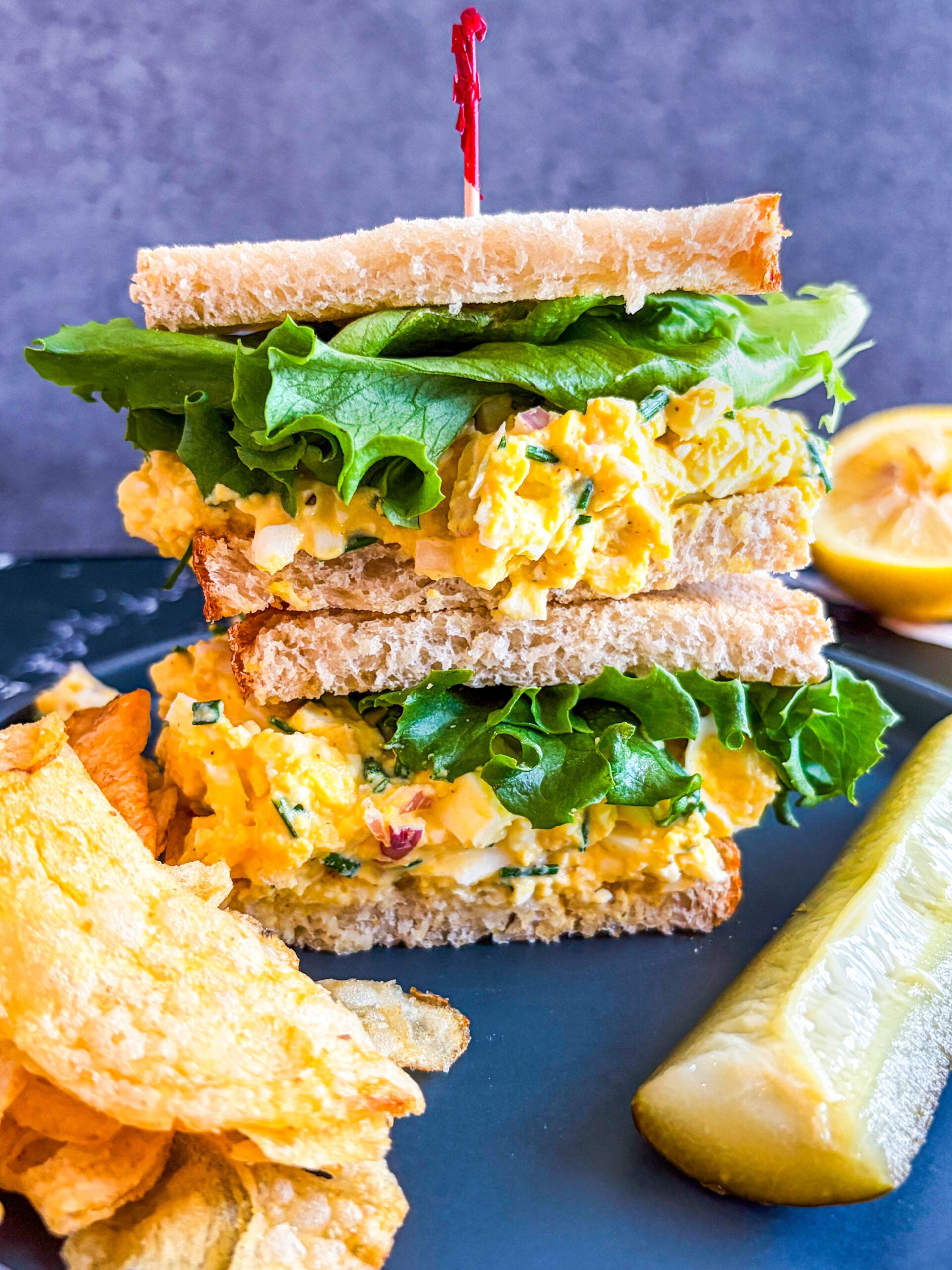 Egg salad sandwich on a plate with pickle and chips