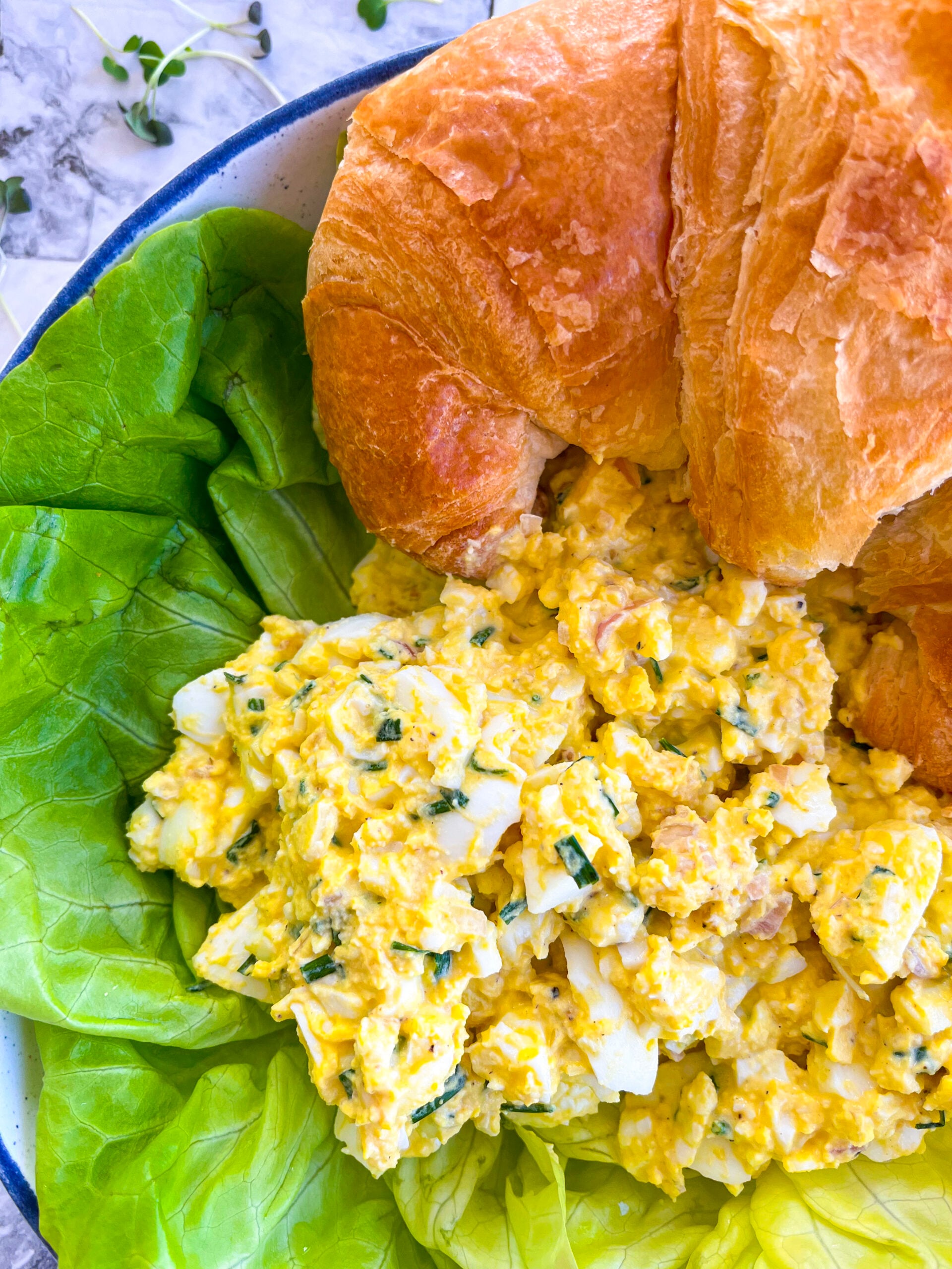 Egg salad on a bed of lettuce next to a croissant