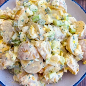 Potato salad in a blue and white serving bowl next to lemon wedge, celery sticks and snipped chives