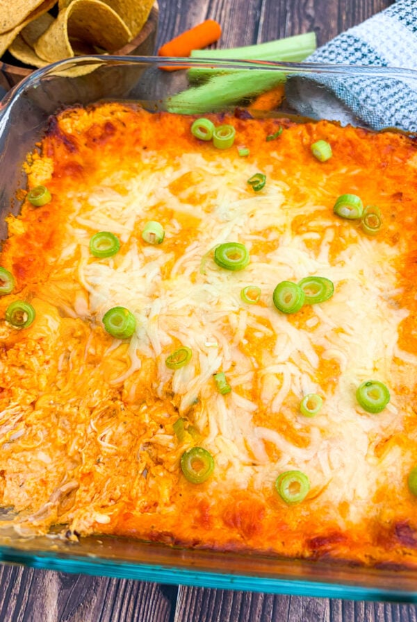 Buffalo chicken dip in a pan garnished with scallion next to chips and veggies