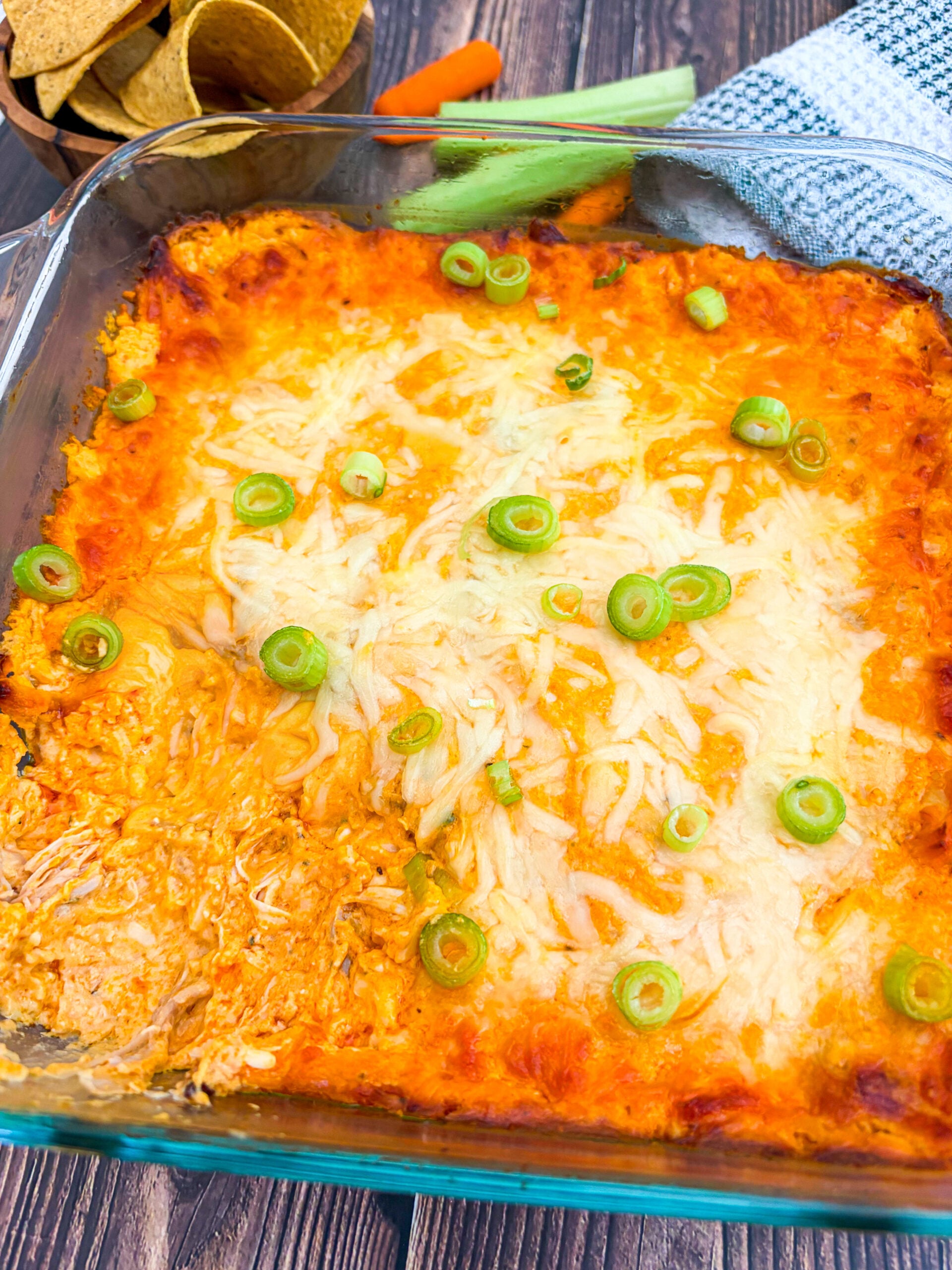 Buffalo chicken dip in a pan garnished with scallion next to chips and veggies