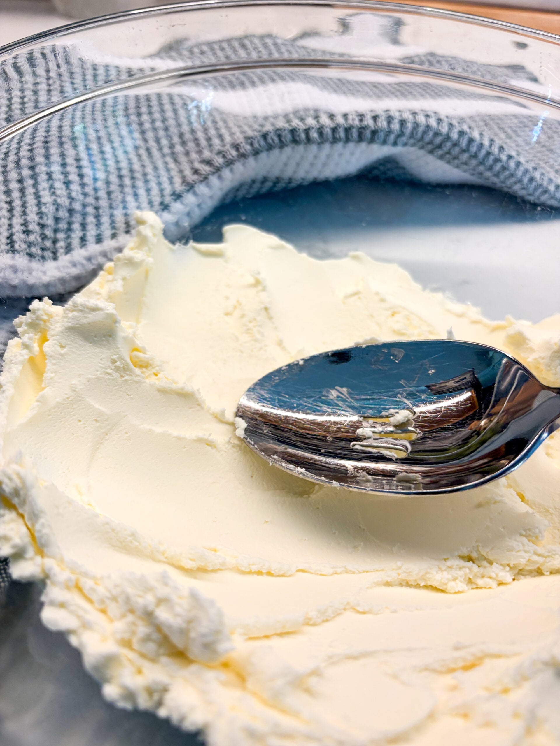 Mashing cream cheese in glass bowl with back of spoon