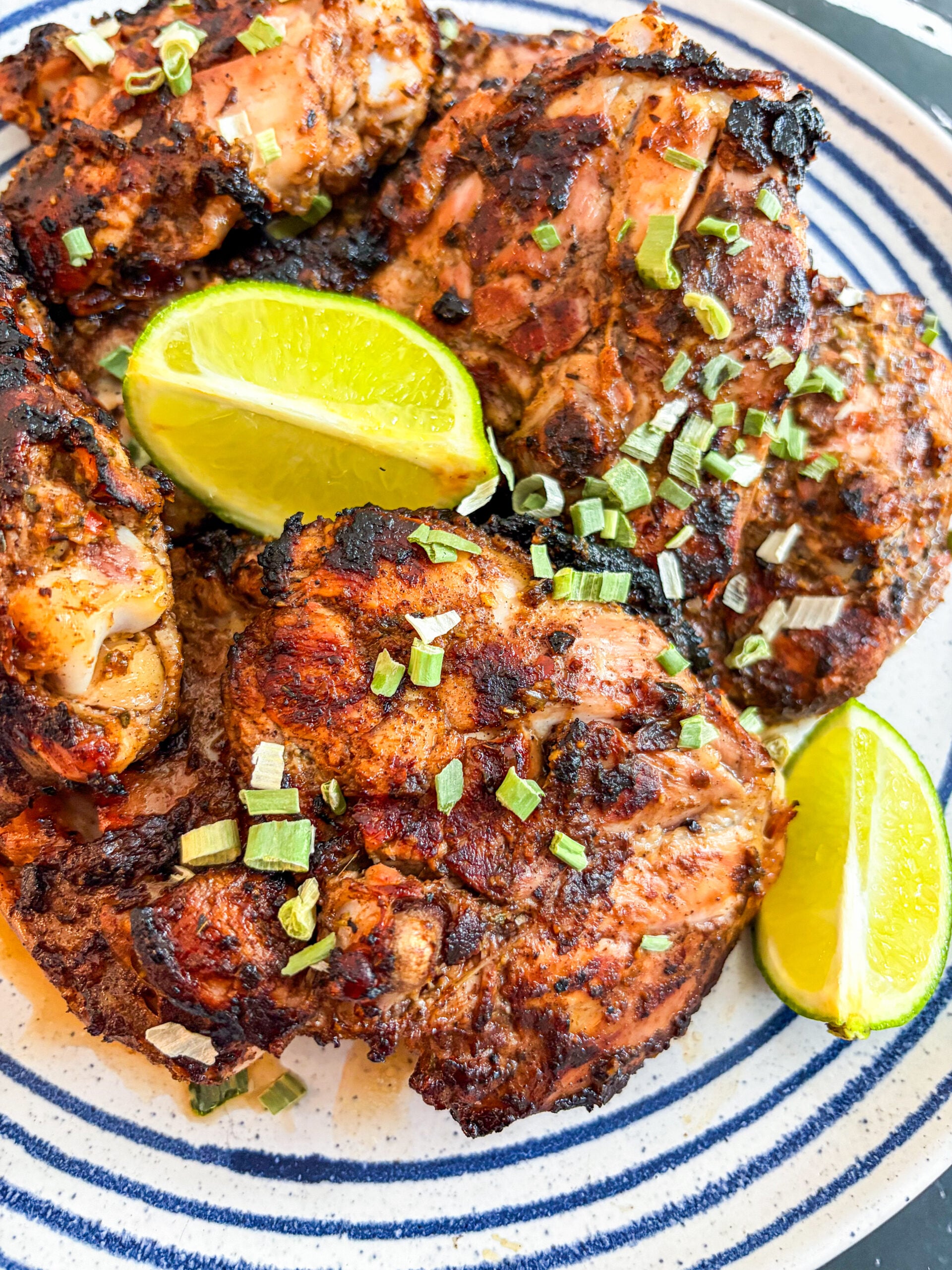 Close up of jerk chicken on blue and white plate garnished with lime wedges and scallions