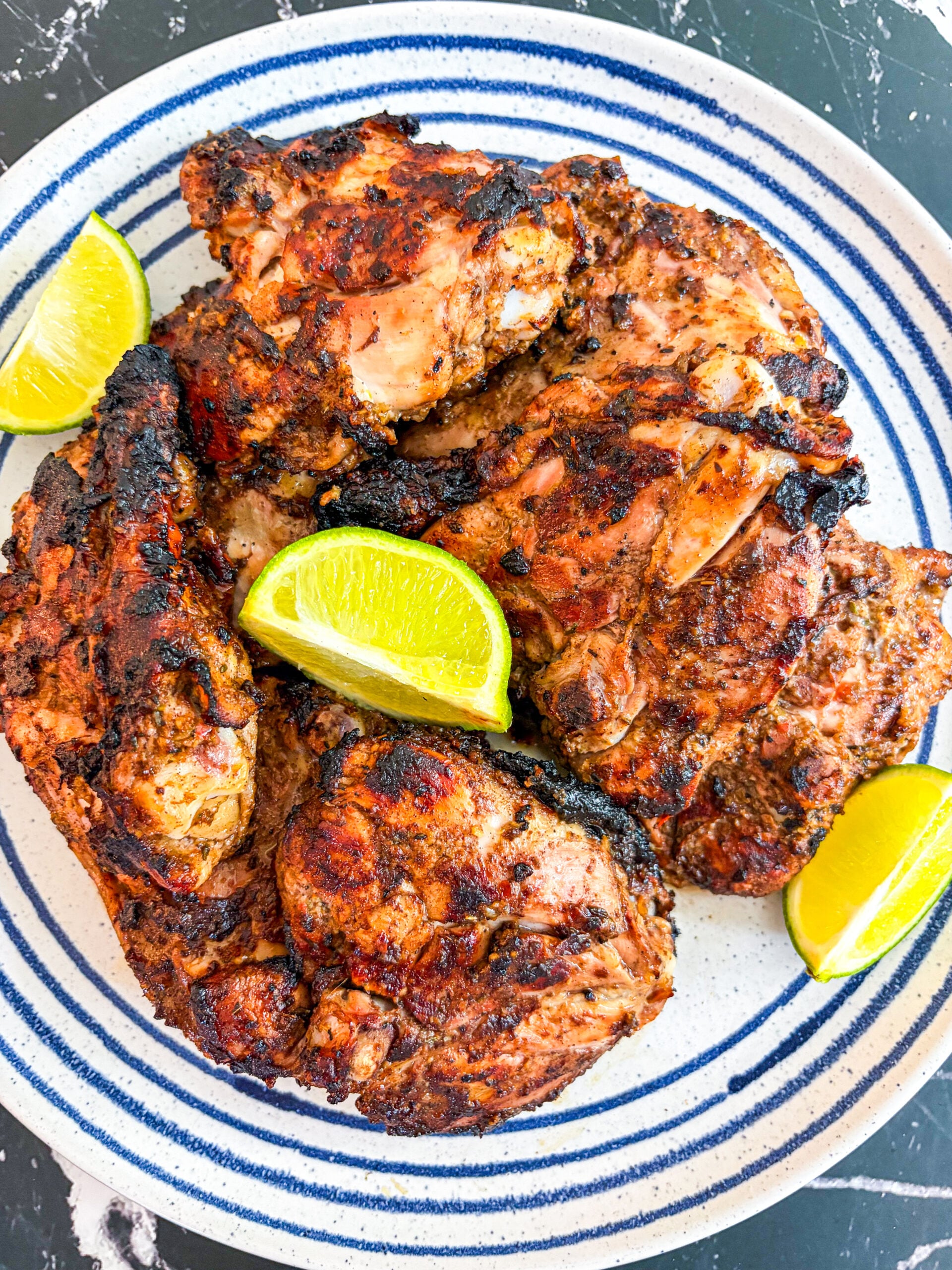 Jerk chicken on blue and white plate with lime wedges