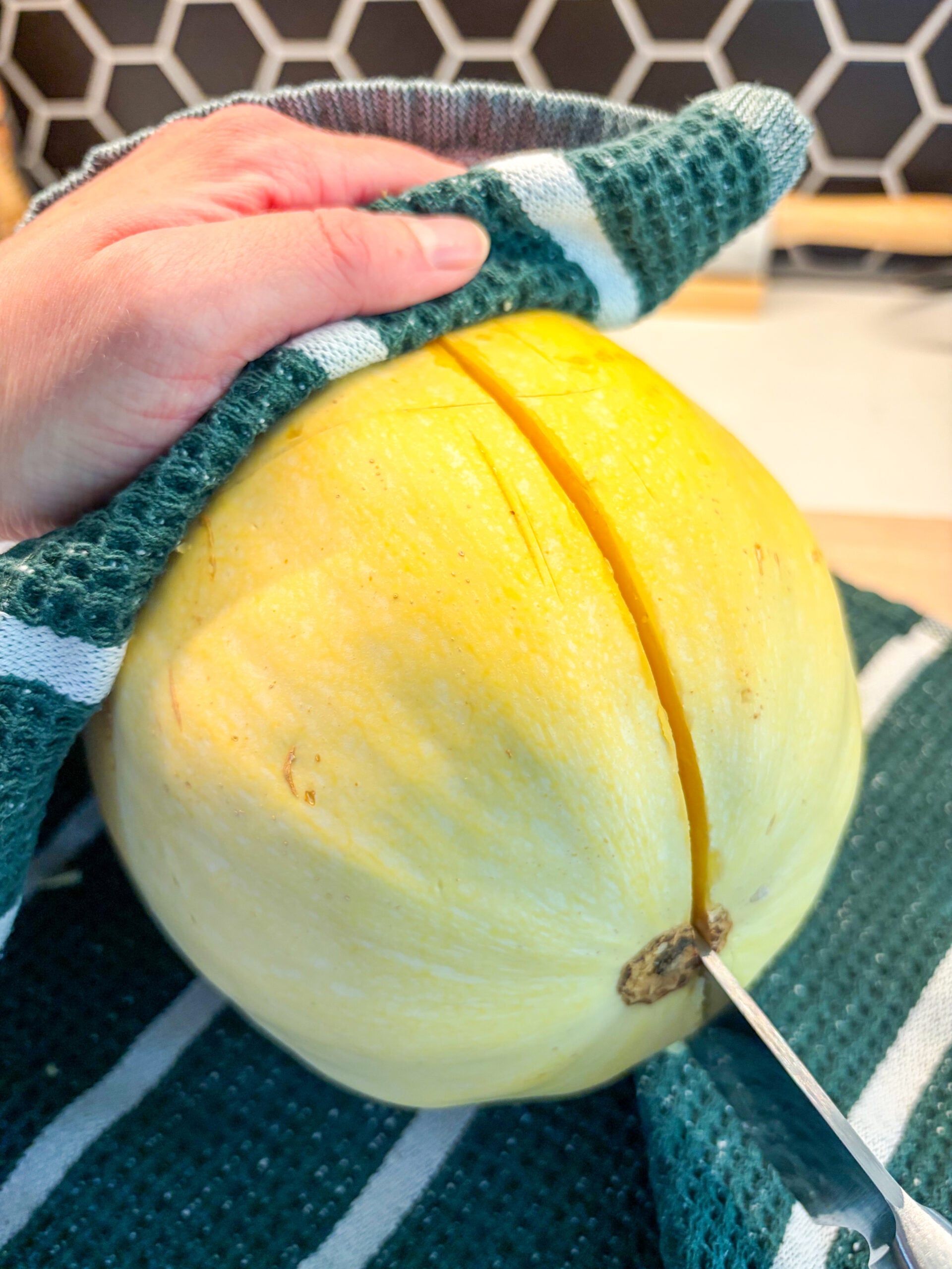 Cutting whole spaghetti squash in half with chef's knife and dish towel