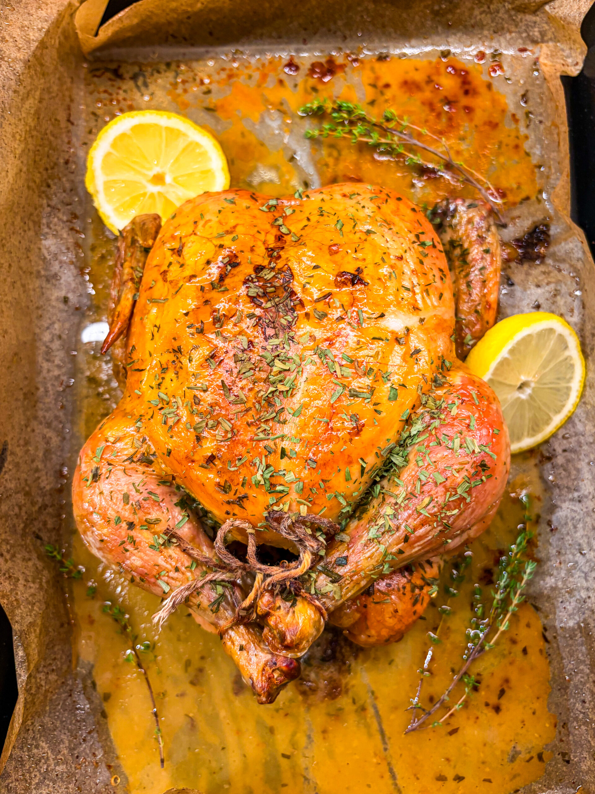 Overhead shot of roast chicken in pan with lemons and herbs