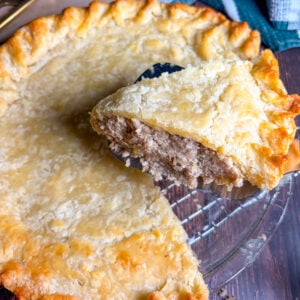 Tourtiere slice held up next to the whole pie