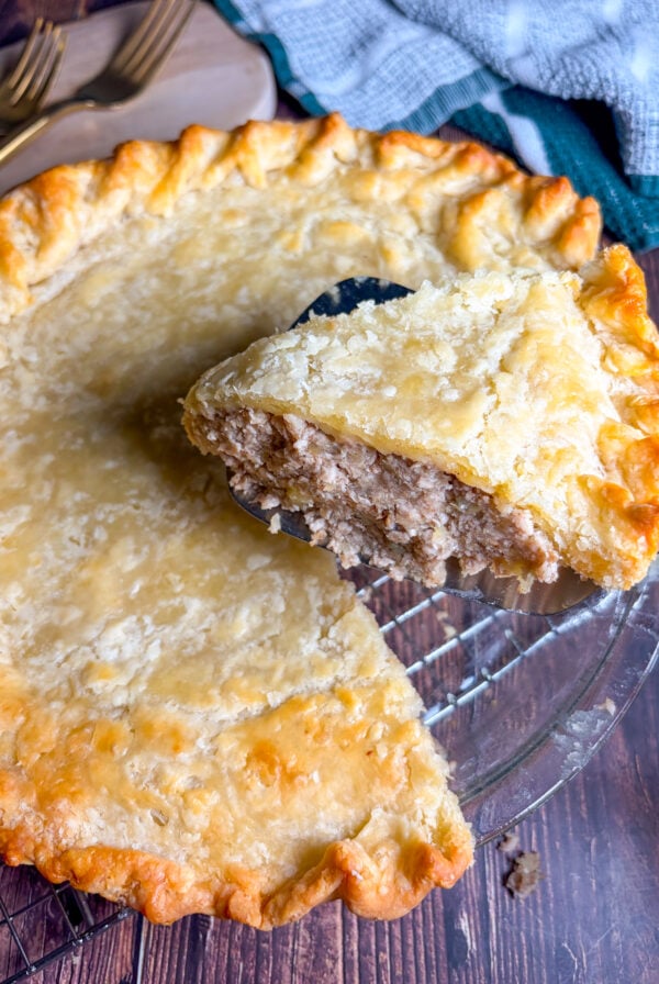 Tourtiere slice held up next to the whole pie