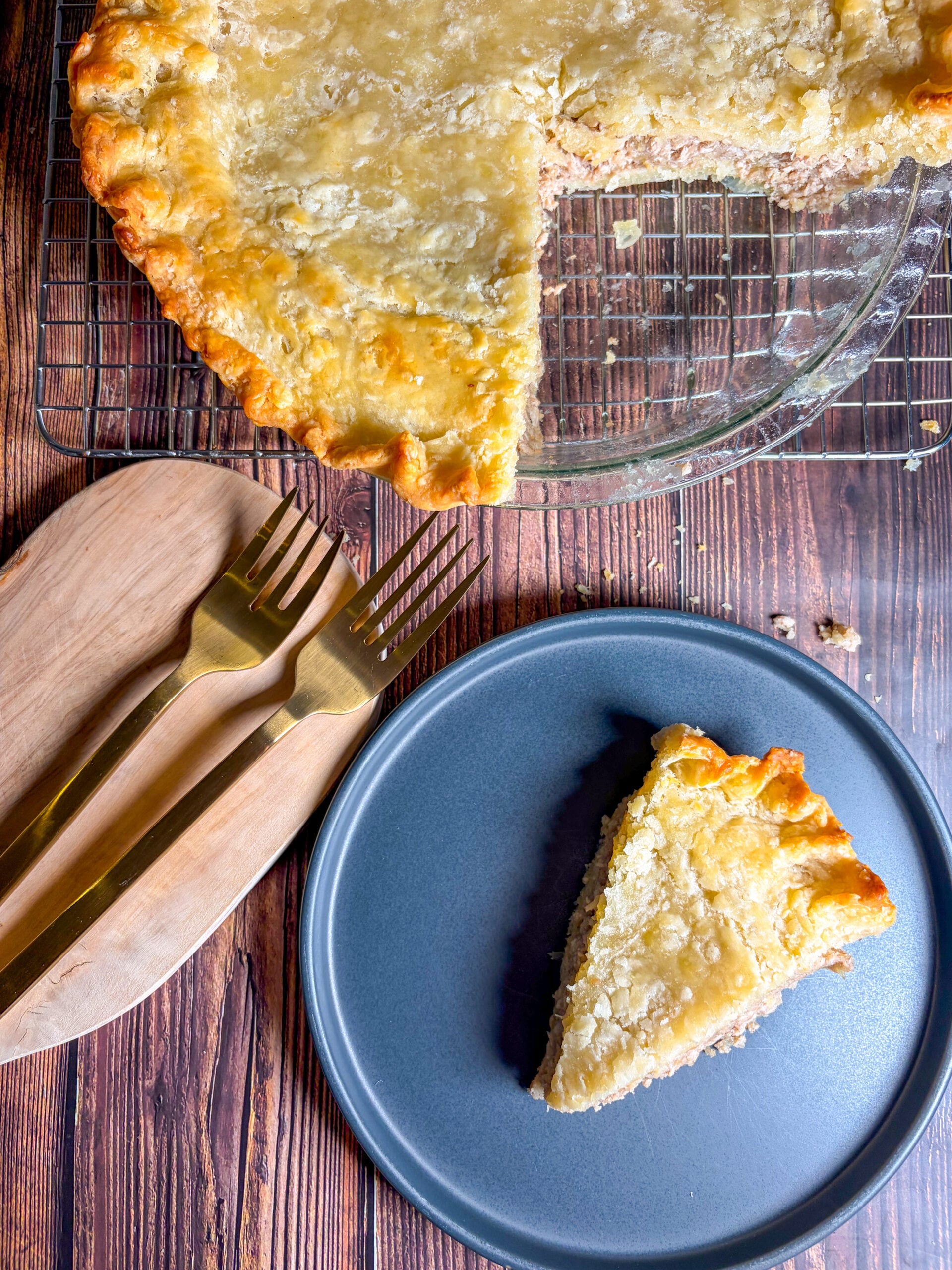 Slice of tourtiere on plate next to full pie and two forks