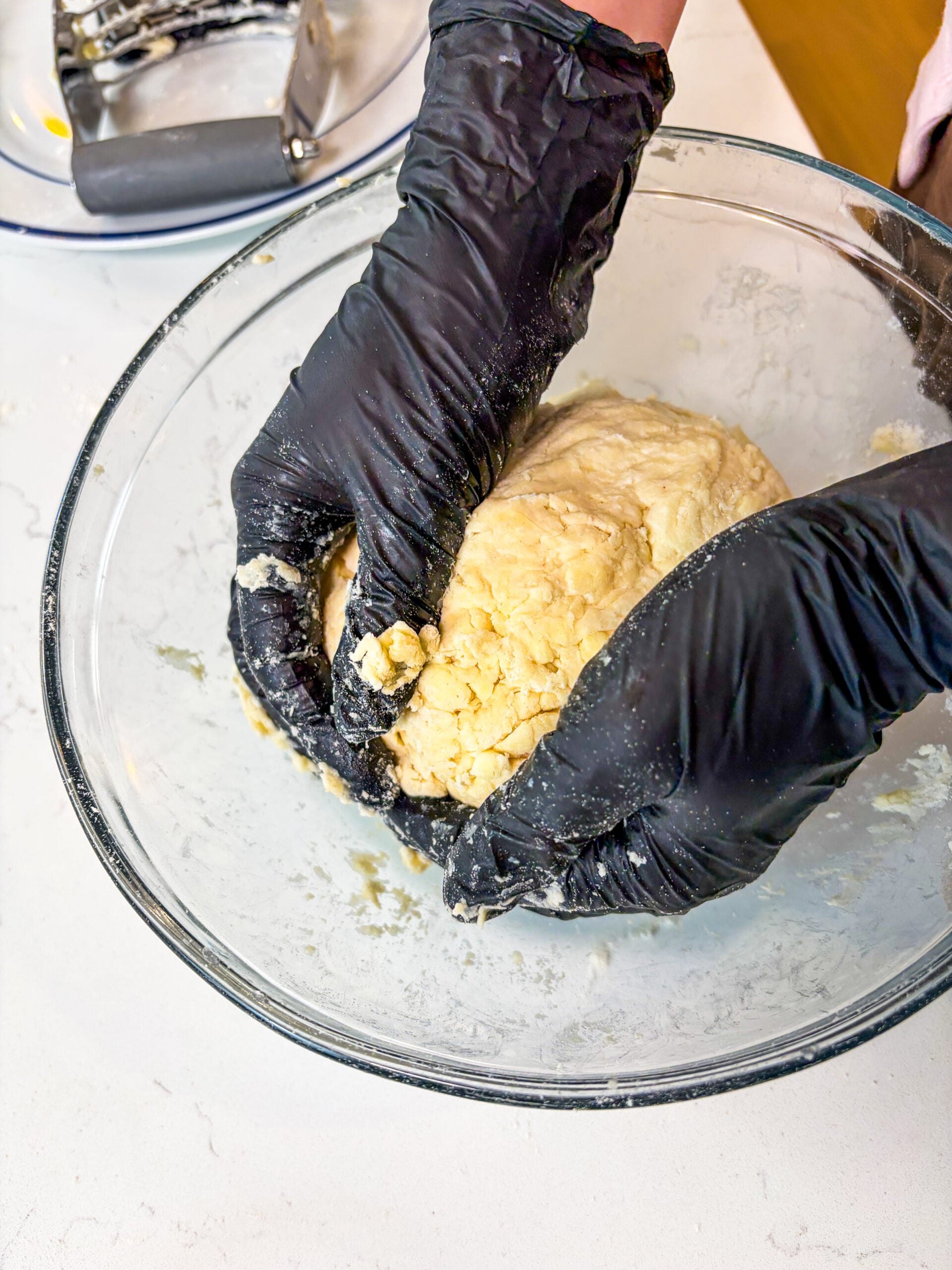 Pie dough being formed into a ball in a glass bowl