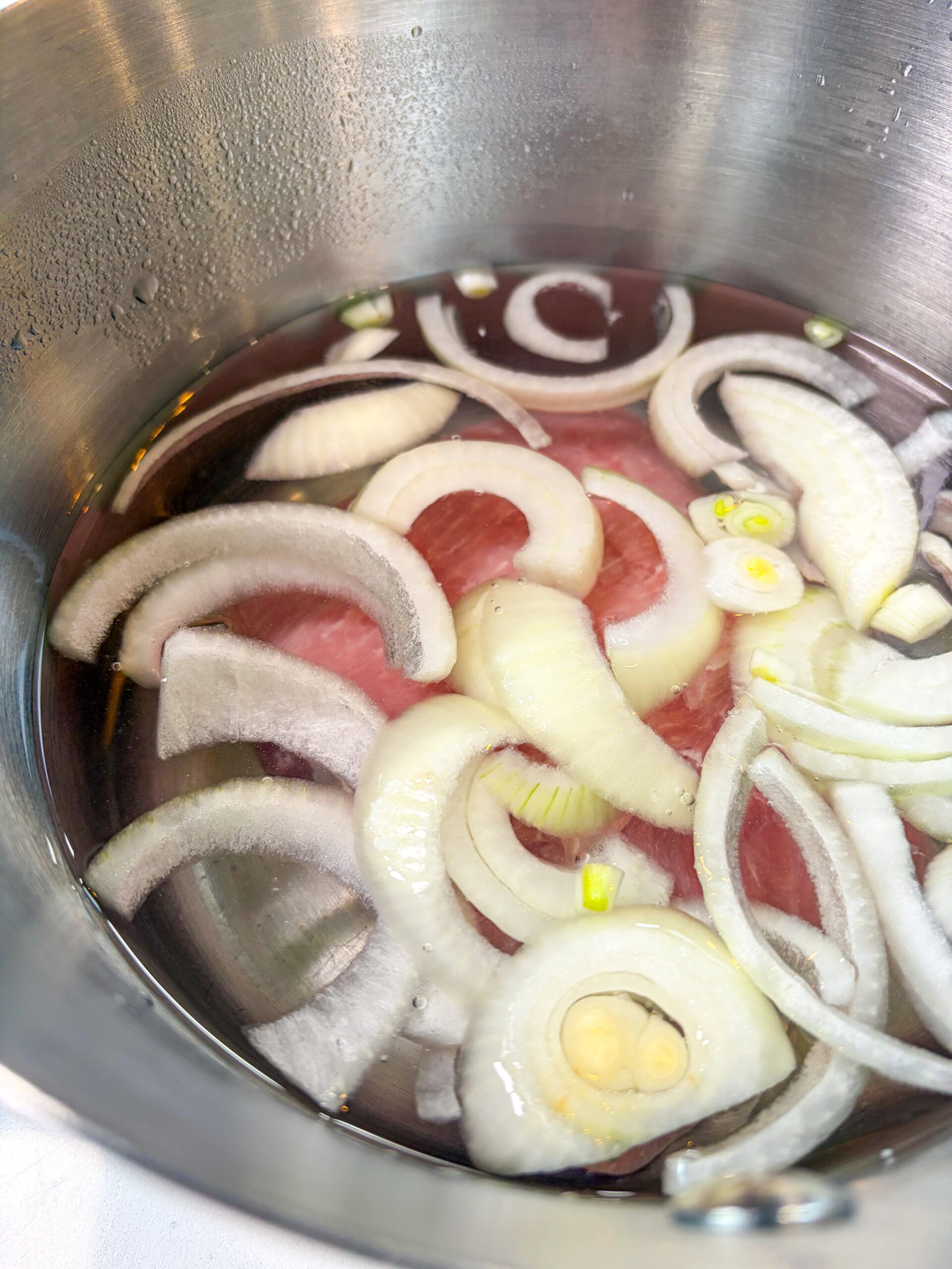 Pork being boiled in water with onion slices
